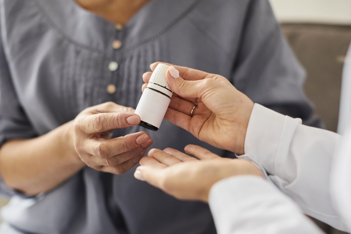 Profissional de saúde entrega frasco de olaparibe a paciente idoso durante consulta médica.