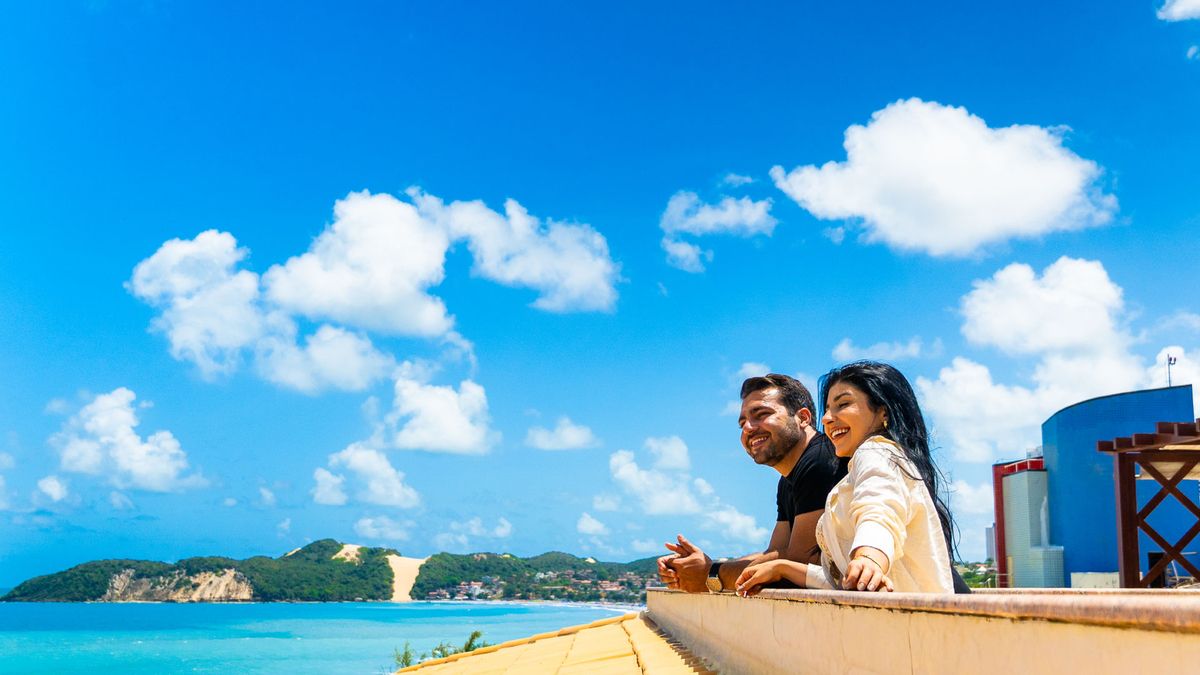 Casal aprecia a vista da varanda do quarto, com o mar e o Morro do Careca ao fundo
